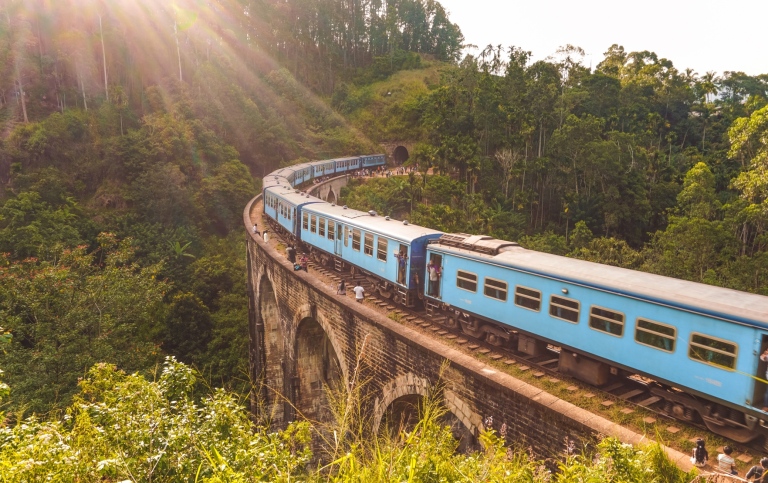 Genre photo: Blue train on an old stone bridge, surrounded by green vegetation, in Sri Lanka.